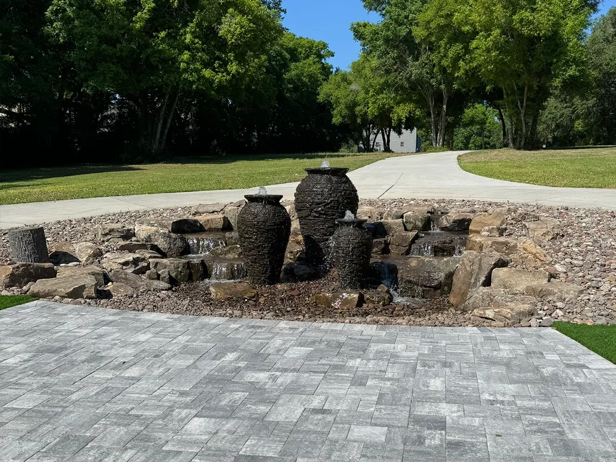 Completed multi-tier fountain with three stone jars in a landscaped garden setting