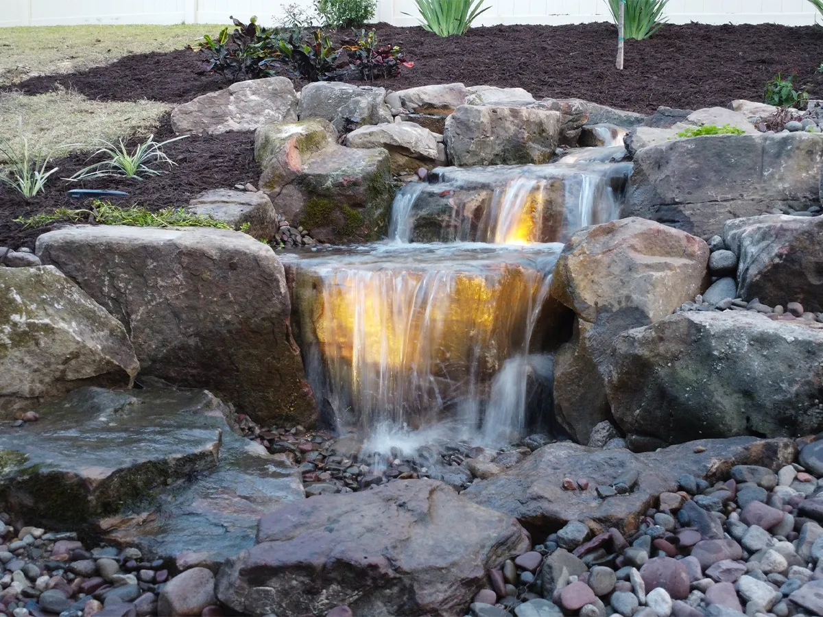 Backyard pondless waterfall with illuminated cascading water and natural rock design.