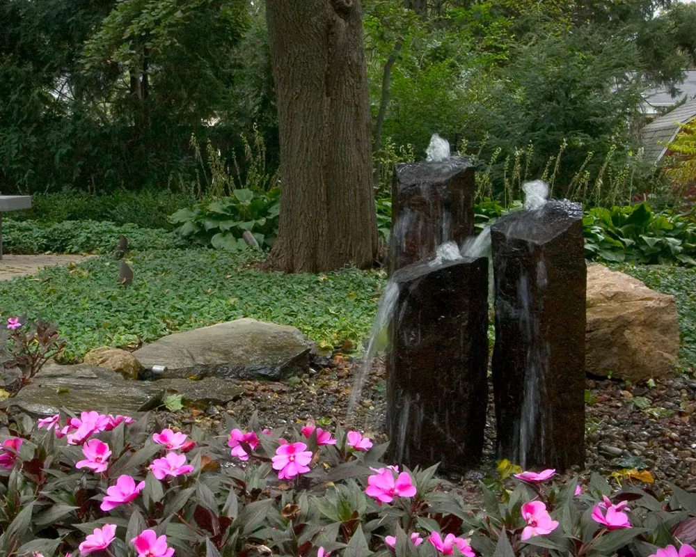 Three stone pillar fountains with water flowing over a natural landscape with pink flowers