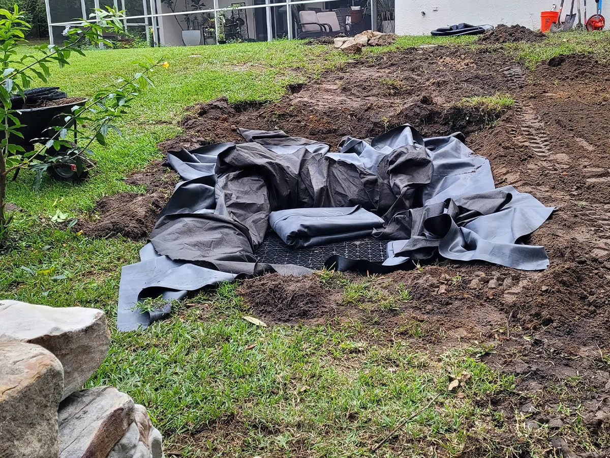 Excavation site for a pondless waterfall with liner materials in a residential backyard.