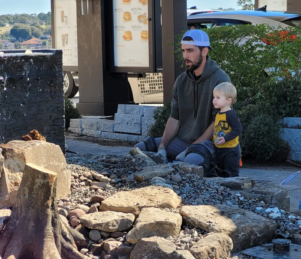 Cameron Perez and son observing a water feature construction project, highlighting family involvement and landscaping work at a public site.