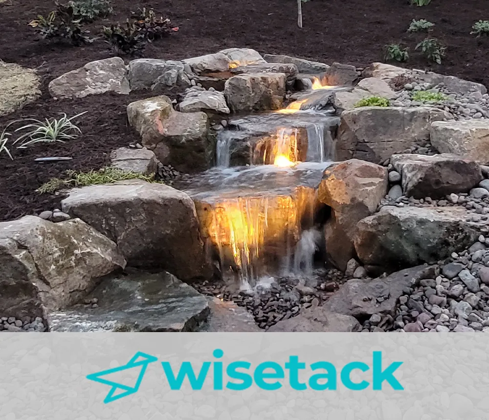 Illuminated waterfall cascading over natural rocks in a landscaped backyard, promoting Wisetack financing options for outdoor projects.