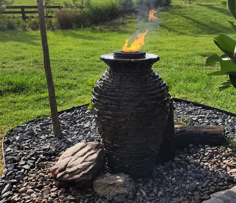 Outdoor fire and water feature fountain with flames, surrounded by rocks and greenery.