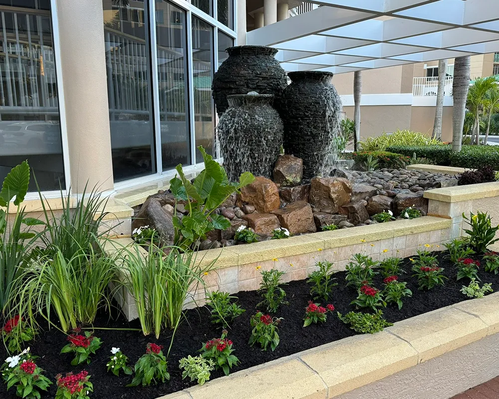 Dual pot water fountains with cascading water and decorative landscaping at a commercial building entrance.