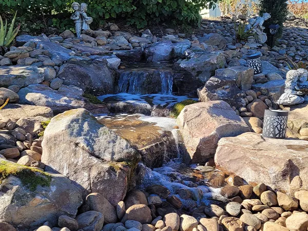 Small backyard waterfall surrounded by decorative rocks and garden statues.