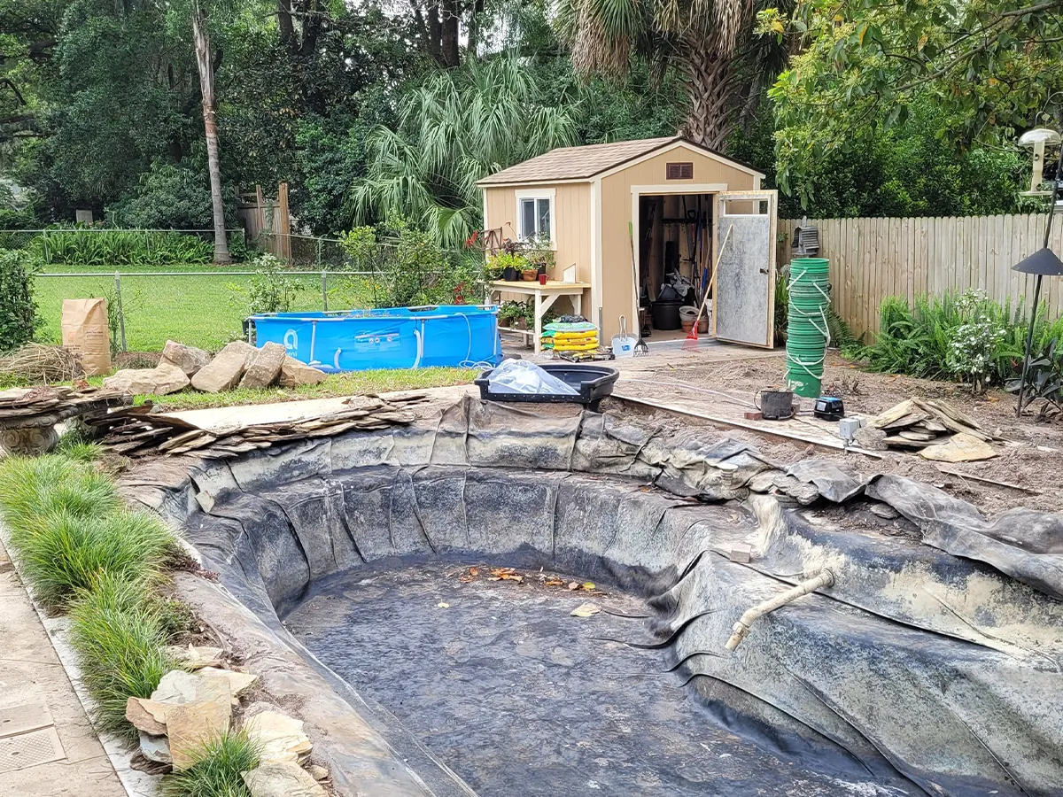 Empty backyard pond with black liner ready for water and landscaping