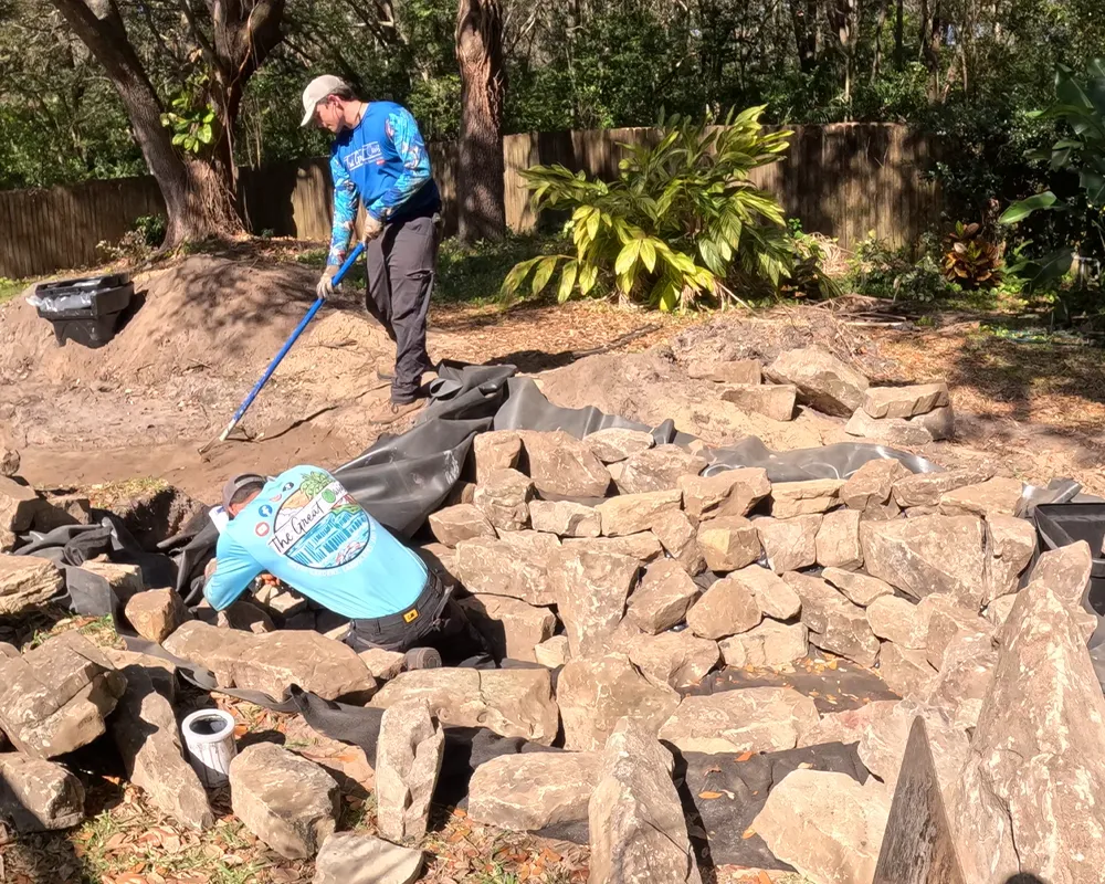 Workers laying stones for a backyard pond installation in a residential garden