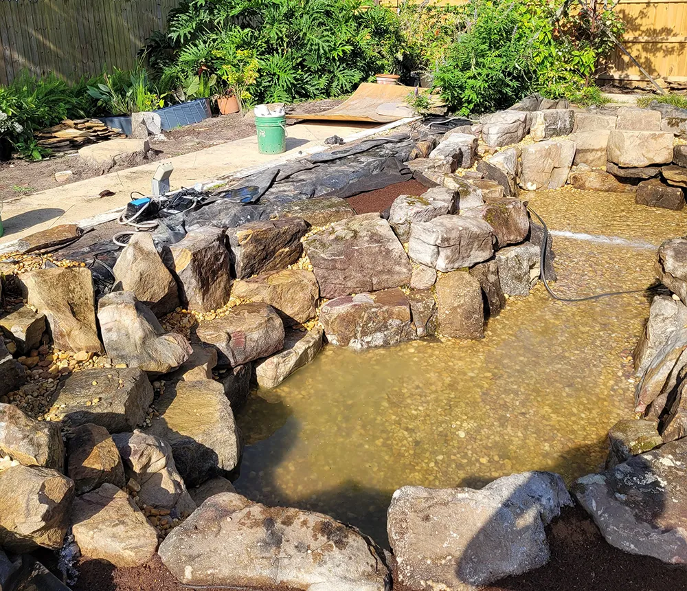 Partially filled backyard pond with natural stone borders under construction