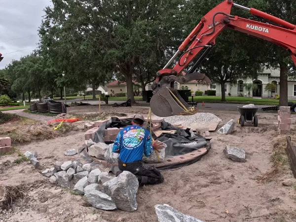 Contractor working on a round fountain base using stones and a mini excavator on-site