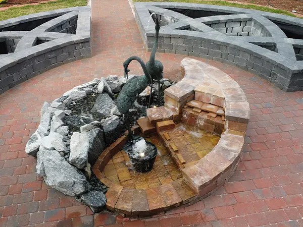 Finished circular fountain with decorative crane statues and water features on a red brick base