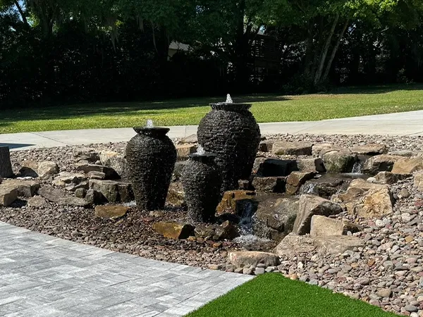 Custom outdoor fountain feature with three water urns surrounded by natural rocks and gravel, creating a modern landscape design.